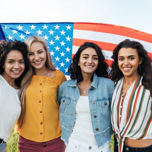 Group of multi-ethnic women holding a USA flag. Female friends celebrating independence day.