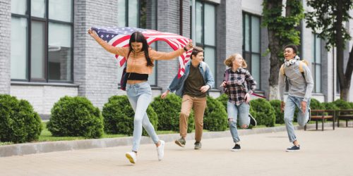 happy teenagers smiling, holding american flag and running outside