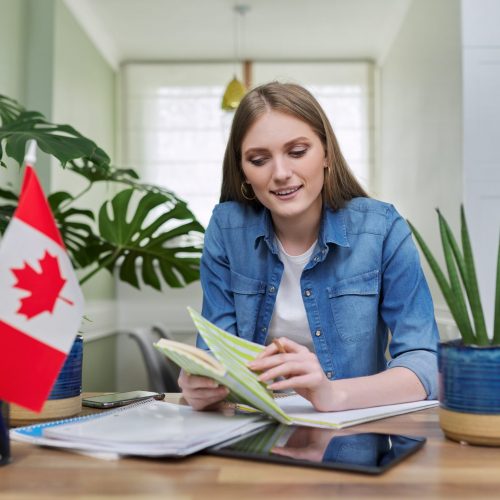 Canada, education, study, students concept. Online training, distance lessons, e-learning, female teenager university student sitting at home looking at webcam, close-up face, Canadian flag on table