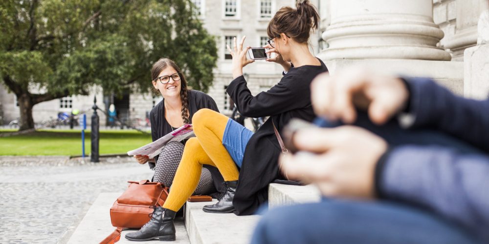 Woman photographing friend while sitting on steps