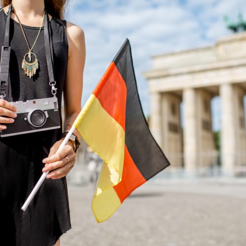 Young woman tourist holding a photo camera and german flag standing in front of the famous Brandenburg gates in Berlin