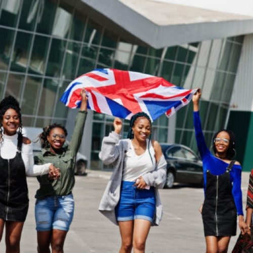 Group of five african american woman walking together on parking with Great Britain flag.