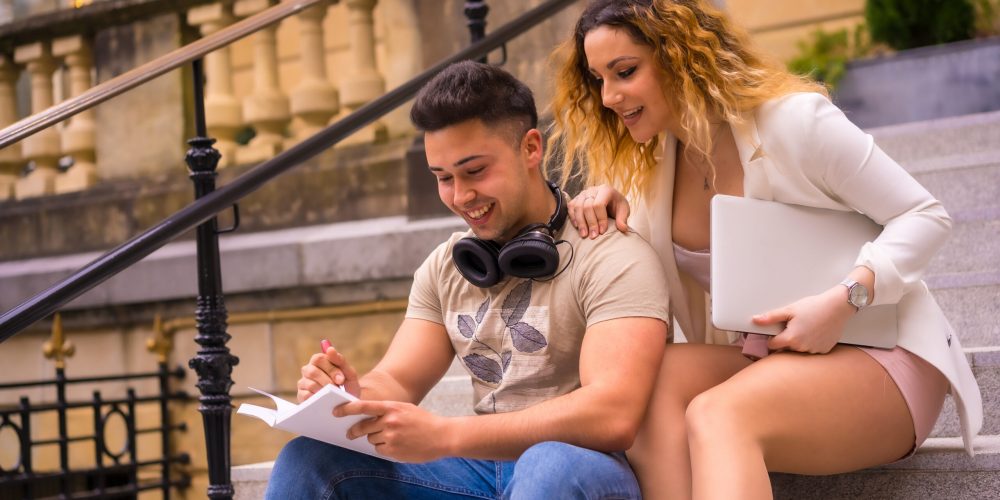 Young entrepreneurs doing teamwork. In the city and with a computer, a boy in headphones and a girl in a white suit